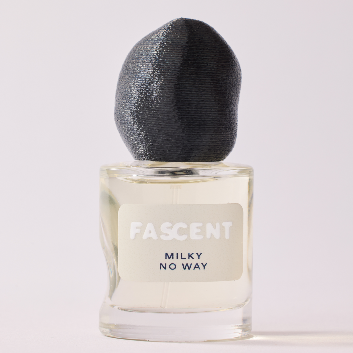 FASCENT Milky No Way perfume bottle with a textured black cap and a clear glass body showing a pale yellow liquid, set against a light off-white background.