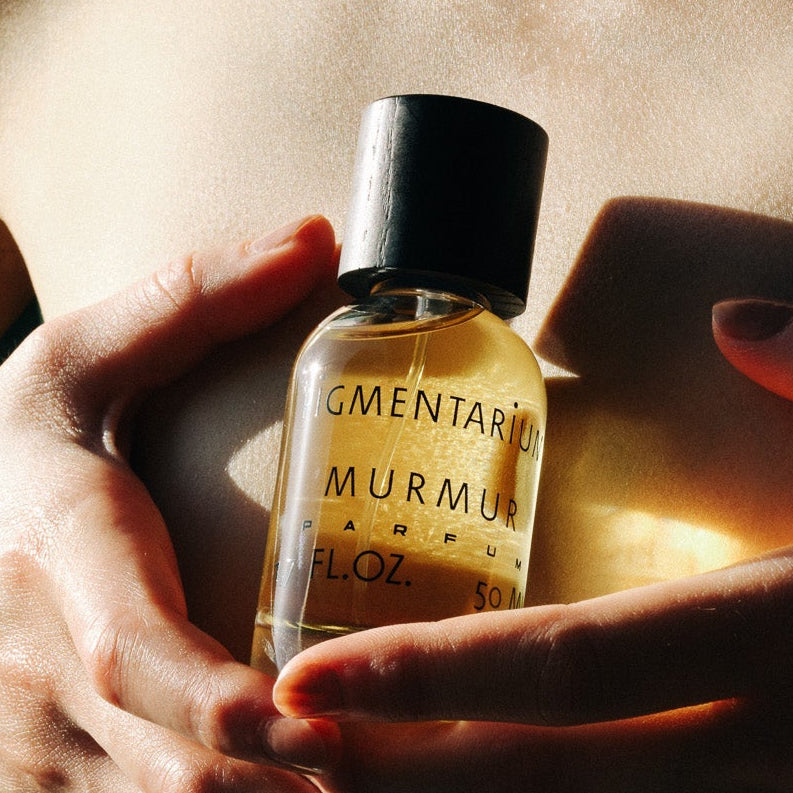 Person holding a bottle labeled Murmur against a dark background