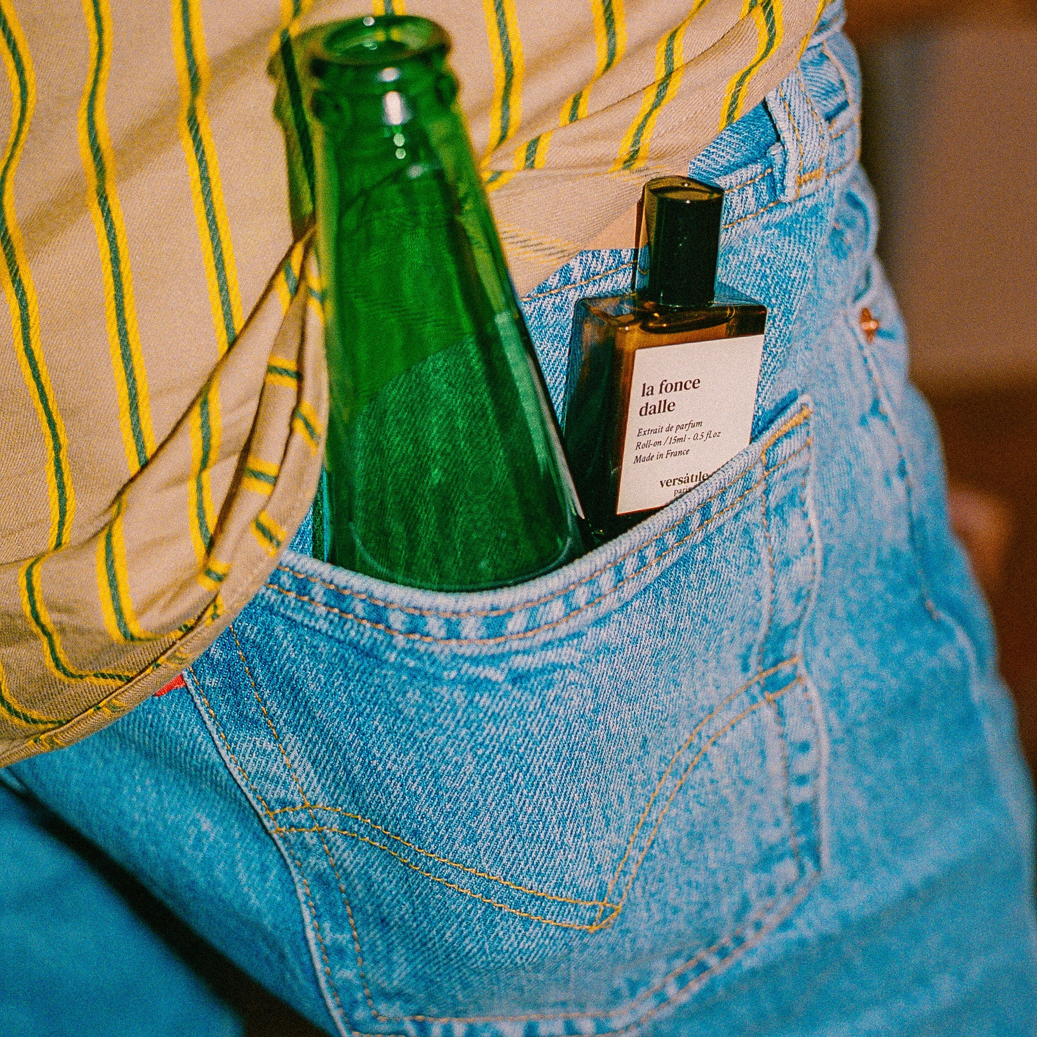 Green bottle and small black bottle with label in a blue pocket of a striped shirt.
