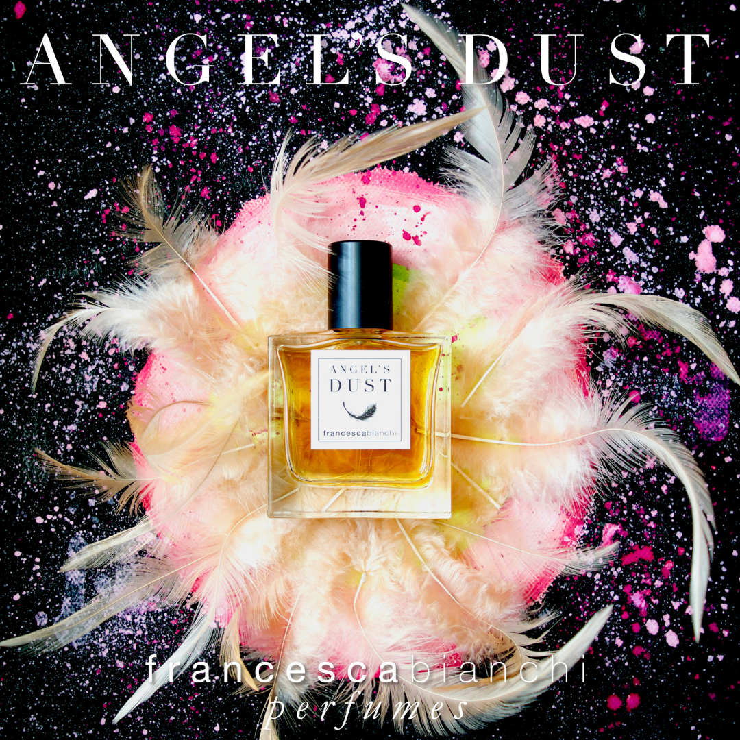 Perfume bottle labeled 'Angels Dust' surrounded by feathers and pink dust on a dark background