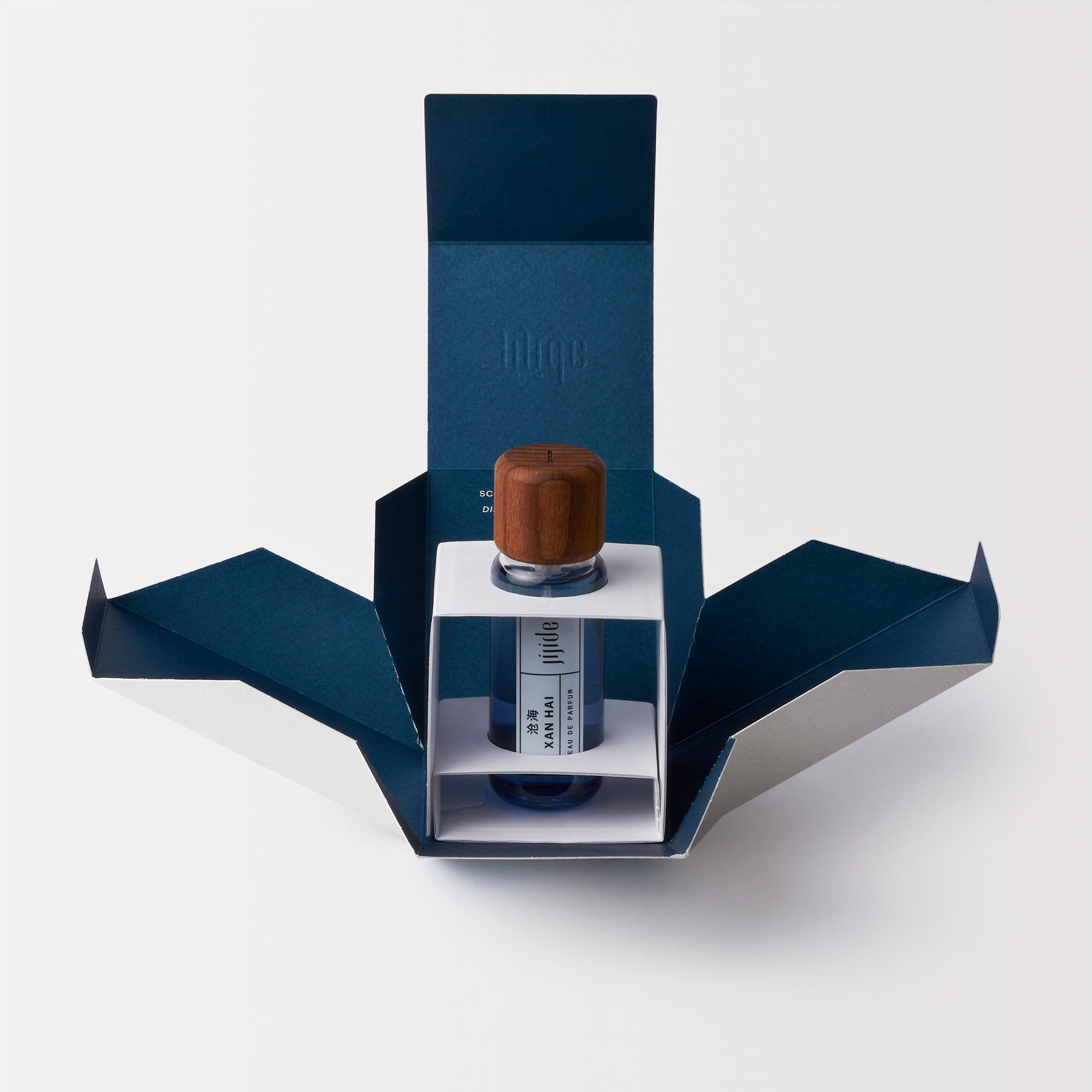 Fragrance bottle with wooden cap in a blue origami-style box on a white background