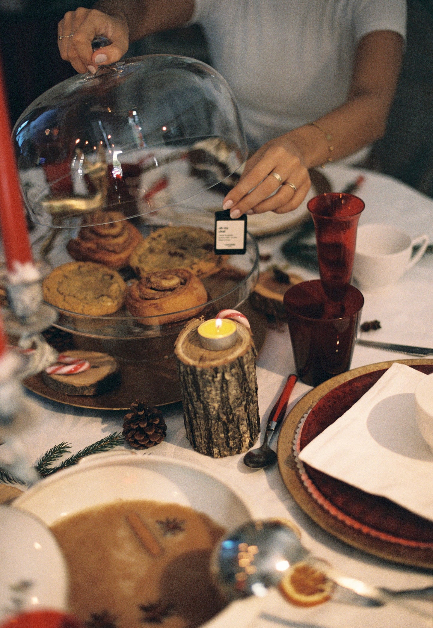 Person holding a glass cloche over a dessert platter on a festive table setting.