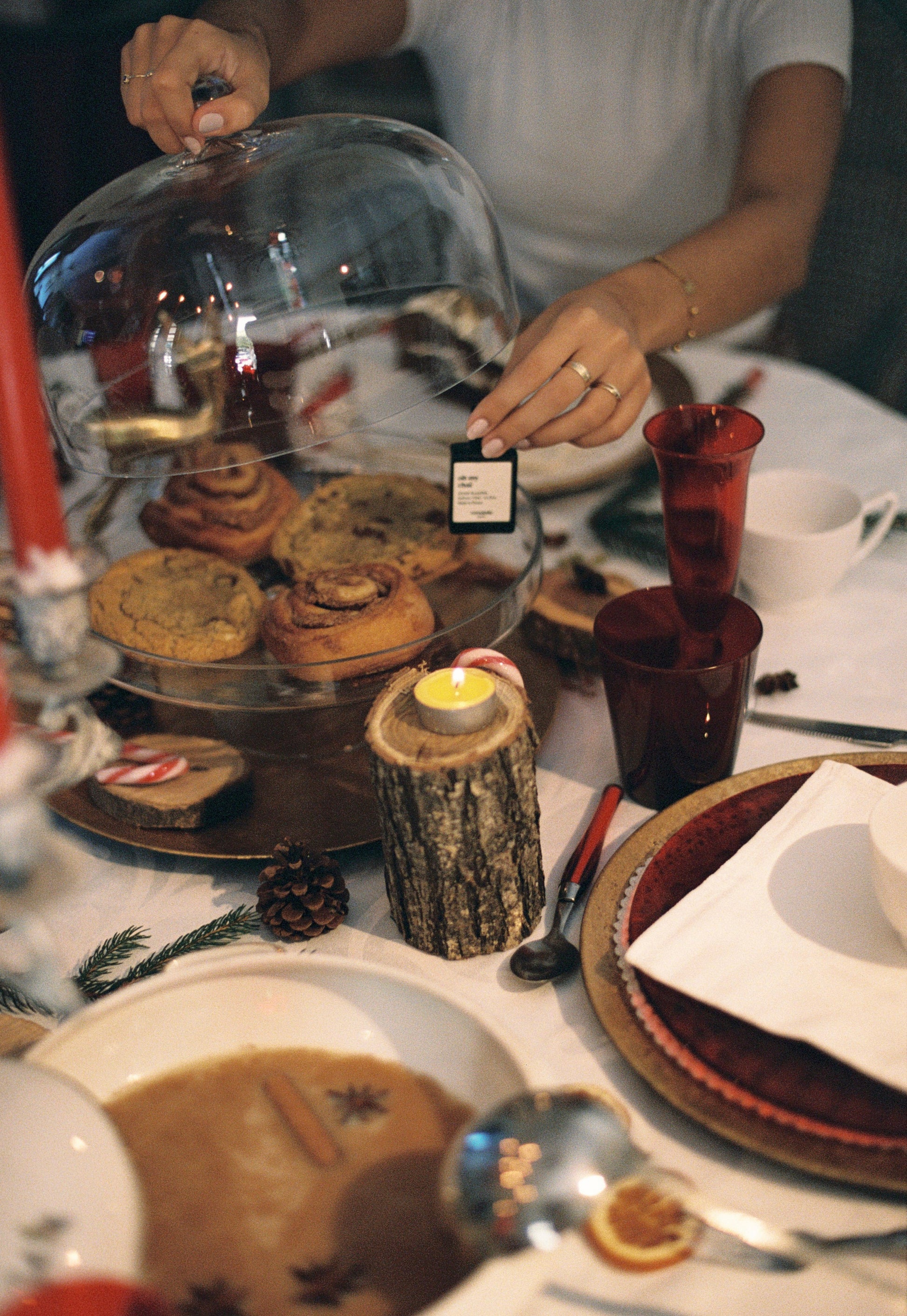 Person holding a glass cloche over a dessert platter on a festive table setting.